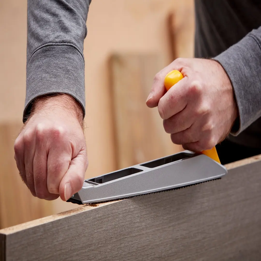 Person glättet Holzkante mit Surformhobel. Personne lisse un bord en bois avec râpe manuelle.